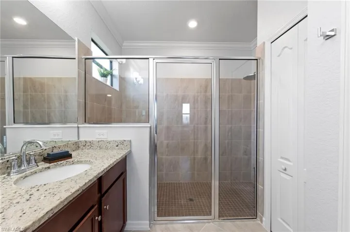 Granite-finish countertop with an undermount sink, wood-finish cabinetry, a glass-enclosed extra-large shower with tiled walls and flooring