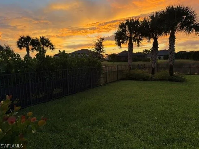 Expansive lawn area with mature palm trees and lush landscaping, enclosed by a black metal fence