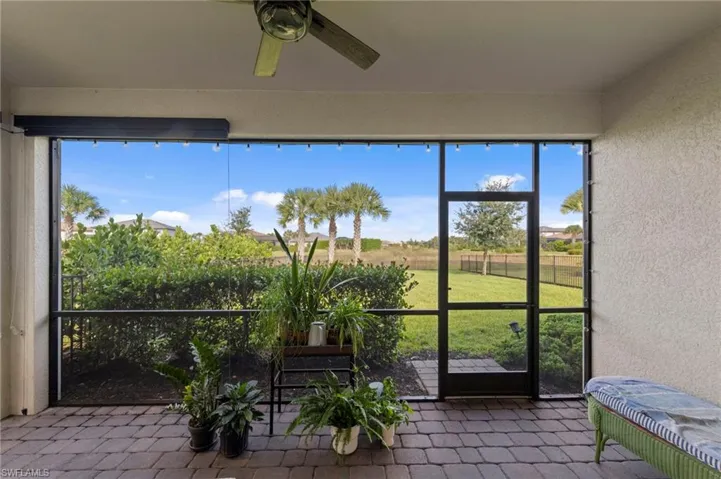 Screened-in lanai featuring a ceiling fan, motorized privacy screens, brick paver flooring, and screen door