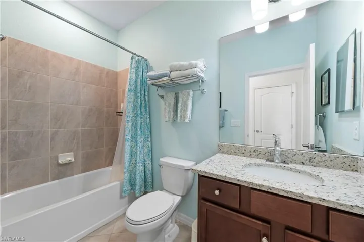 White bathtub with tile surround, wood-finish vanity with an integrated sink, polished chrome faucet, and expansive wall-mounted mirror