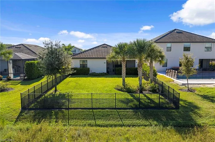 Expansive backyard featuring a manicured lawn, perimeter fencing, and mature palm trees