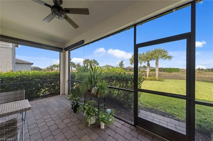 Screened lanai featuring a ceiling fan, motorized privacy screens, paver flooring, and mature landscaping