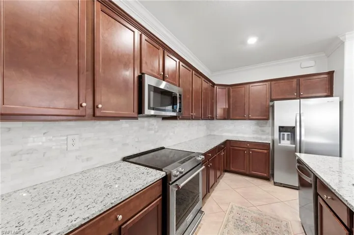 Kitchen featuring wood-finish cabinetry, stainless steel appliances, granite countertops, and a subway tile backsplash