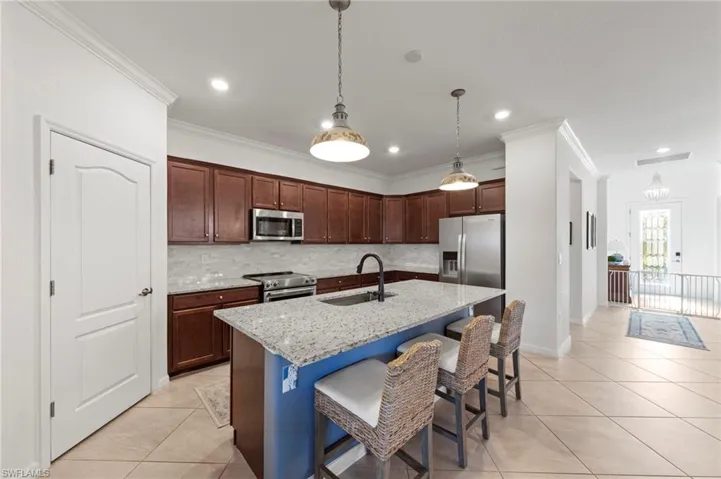 Kitchen featuring wood cabinetry, stainless steel appliances, a center island with a light-toned countertop, and tile flooring