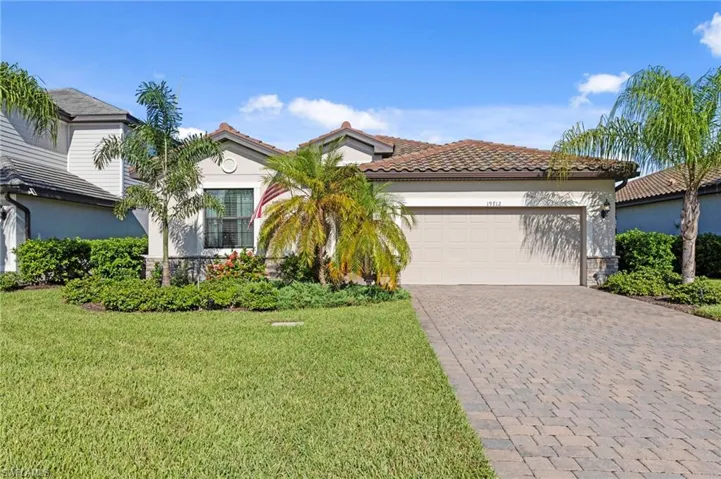Mediterranean-style exterior featuring a tile roof, paver driveway, attached garage, and mature landscaping