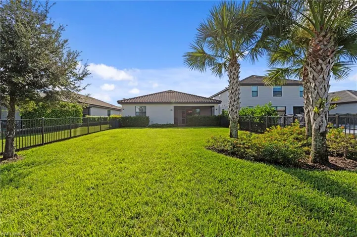 Expansive fenced backyard featuring a manicured lawn, mature palm trees, and established landscaping. Room for a pool and great for pets or children.