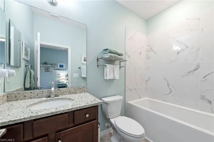 Upgraded soaker tub with white tile surround, dark wood-finish vanity with stone countertop, and an integrated sink with a chrome faucet