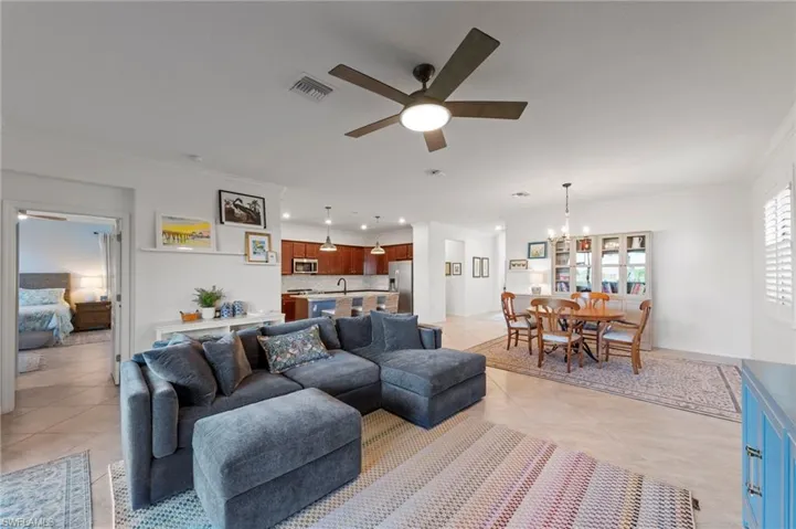 Open-concept living area featuring light-toned tile flooring, a dining area with a chandelier, and a kitchen with warm wood-finish cabinetry