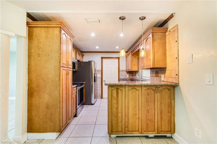 Kitchen featuring light stone counters, decorative light fixtures, stainless steel appliances, a peninsula, and brown cabinetry