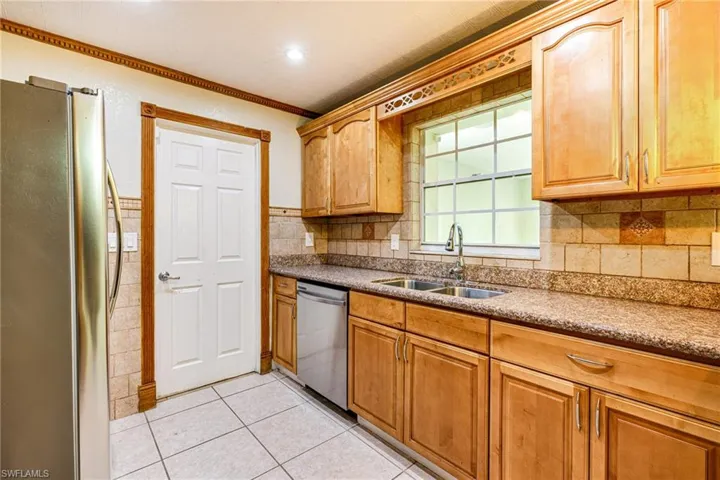 Kitchen featuring appliances with stainless steel finishes, crown molding, light stone counters, light tile patterned floors, and brown cabinets