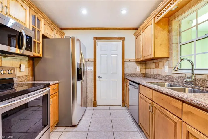 Kitchen featuring appliances with stainless steel finishes, light stone counters, ornamental molding, glass insert cabinets, and light tile patterned flooring