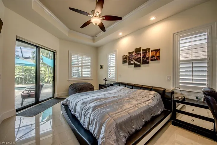 Bedroom featuring ornamental molding, access to exterior, light tile patterned floors, a tray ceiling, and a ceiling fan