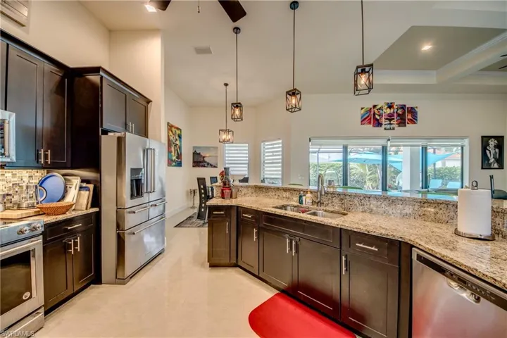Kitchen with dark brown cabinets, appliances with stainless steel finishes, pendant lighting, and light stone counters