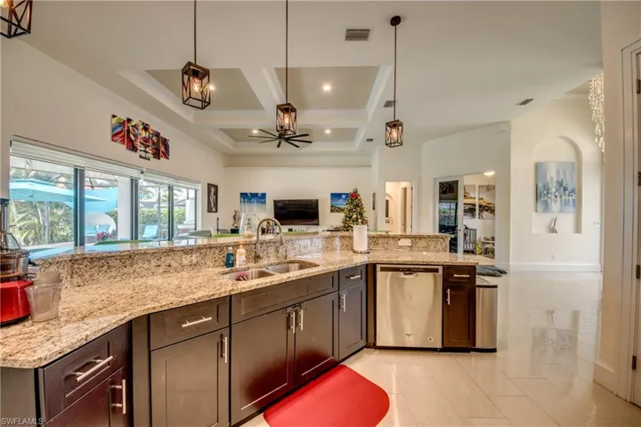 Kitchen featuring hanging light fixtures, open floor plan, light stone countertops, coffered ceiling, and dishwasher