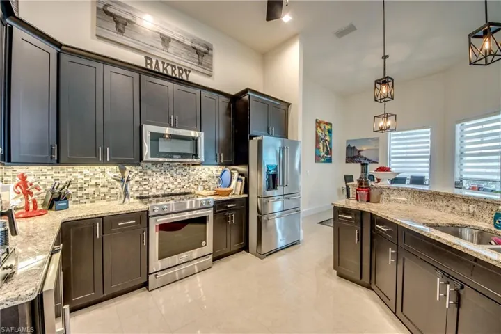 Kitchen featuring appliances with stainless steel finishes, light stone counters, decorative light fixtures, decorative backsplash, and beverage cooler