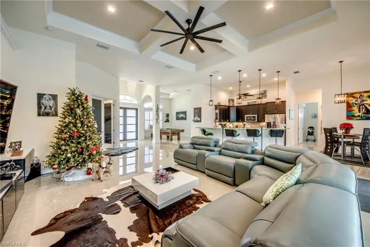 Living room with coffered ceiling, a high ceiling, a ceiling fan, beamed ceiling, and crown molding