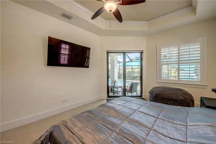 Bedroom featuring a raised ceiling, access to outside, ornamental molding, a ceiling fan, and carpet