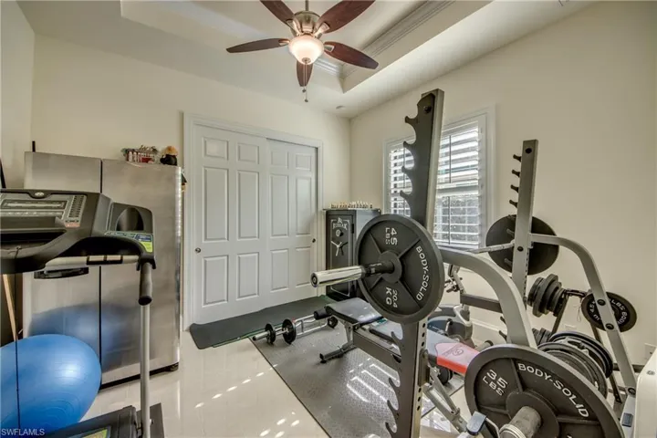 Workout area featuring a tray ceiling, crown molding, a ceiling fan, and tile patterned flooring