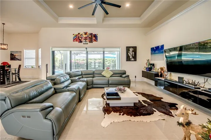 Living room featuring light tile patterned floors, a high ceiling, coffered ceiling, crown molding, and ceiling fan