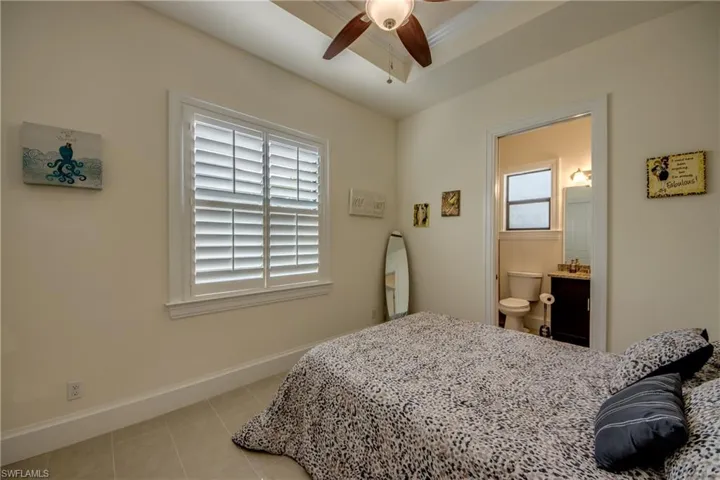 Bedroom with light tile patterned floors, a ceiling fan, a raised ceiling, and connected bathroom