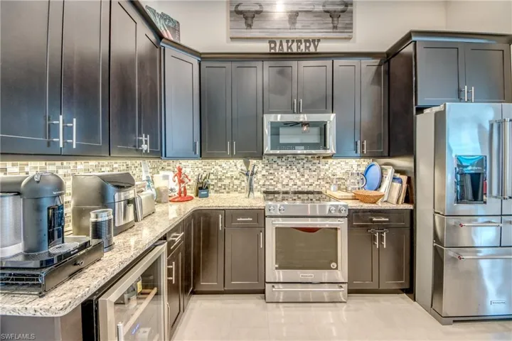 Kitchen featuring high end appliances, beverage cooler, light stone countertops, backsplash, and light tile patterned floors