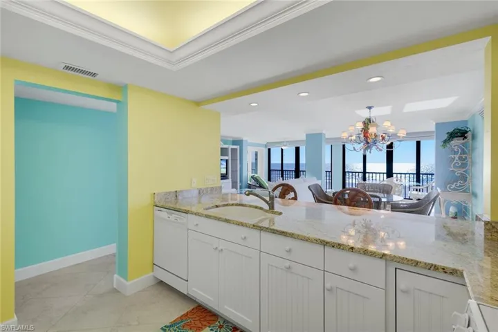 Kitchen with light stone countertops, crown molding, a chandelier, white appliances, and plenty of natural light