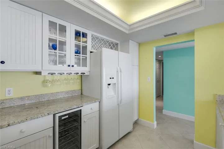 Kitchen with glass fronted cabinets, white cabinetry, light stone countertops, and wine cooler