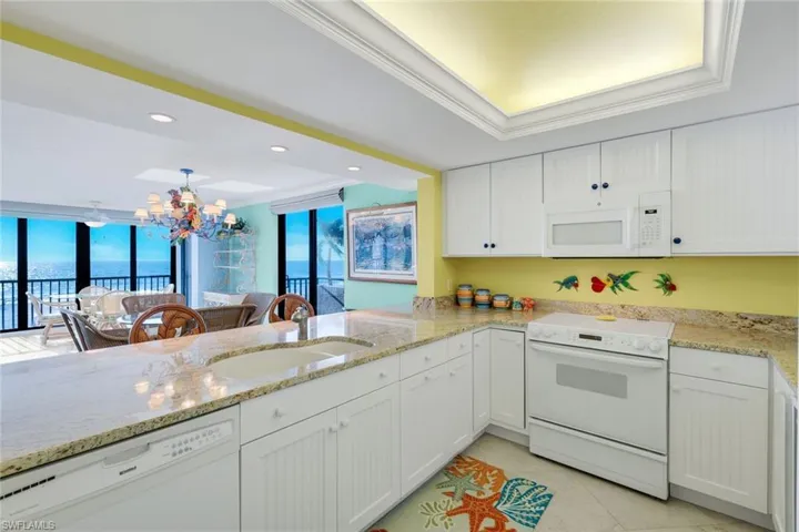 Kitchen featuring white appliances, ornamental molding, white cabinets, light stone counters, and suspended lighting