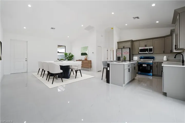 Kitchen featuring appliances with stainless steel finishes, gray cabinets, a kitchen bar, a center island, and high vaulted ceiling