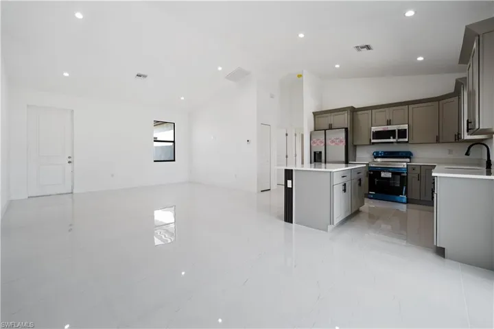 Kitchen featuring appliances with stainless steel finishes, open floor plan, gray cabinetry, high vaulted ceiling, and a center island