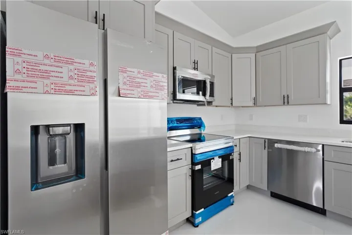 Kitchen with stainless steel appliances, gray cabinets, and light tile patterned floors