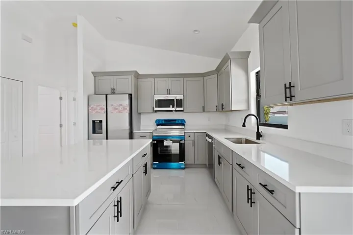 Kitchen featuring gray cabinets, appliances with stainless steel finishes, a kitchen island, lofted ceiling, and light stone countertops