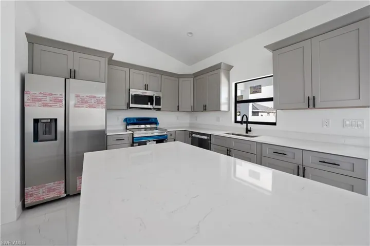 Kitchen with gray cabinets, stainless steel appliances, light stone counters, lofted ceiling, and light marble finish flooring