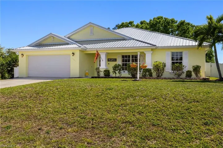 View of front of property with driveway, stucco siding, a front lawn, a garage, and metal roof