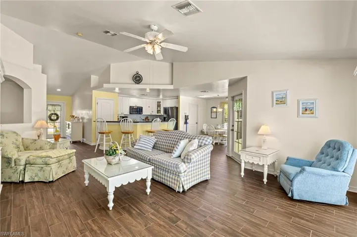 Living area with wood finish floors, visible vents, lofted ceiling, and a ceiling fan