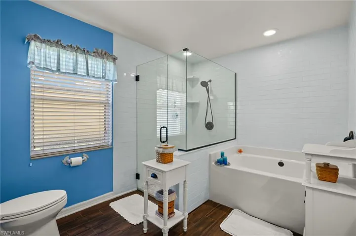 Bathroom with wood finish floors, toilet, a bath, and a tile shower
