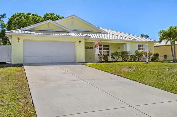 Ranch-style house with a front yard, driveway, a standing seam roof, an attached garage, and stucco siding