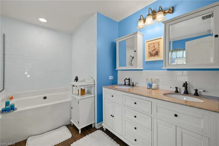 Bathroom with decorative backsplash, a tub, visible vents, and a sink