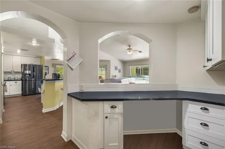 Kitchen with dark wood-type flooring, black fridge with ice dispenser, dark countertops, arched walkways, and white cabinets