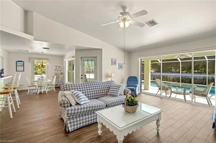 Living area featuring wood finished floors, ceiling fan with notable chandelier, visible vents, and vaulted ceiling