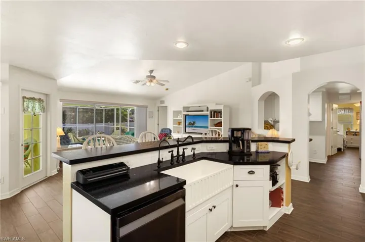 Kitchen featuring dark wood-type flooring, ceiling fan, lofted ceiling, arched walkways, and a kitchen island with sink