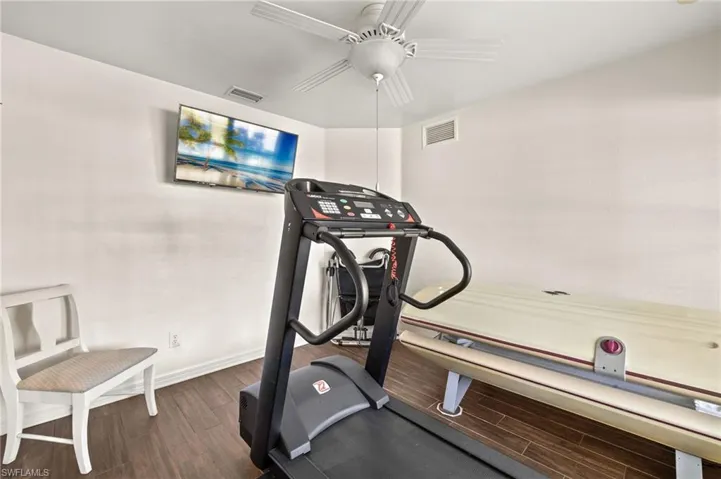 Exercise area with ceiling fan, visible vents, baseboards, and wood finished floors