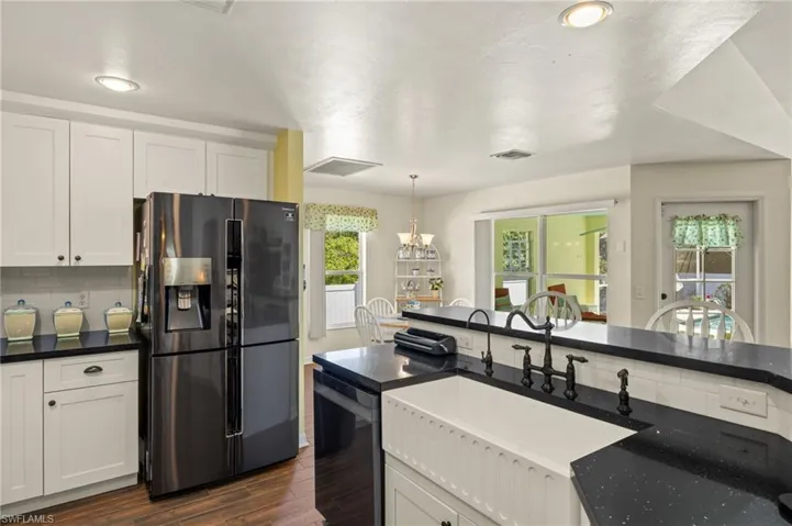 Kitchen with visible vents, dark wood finished floors, a sink, black appliances, and backsplash