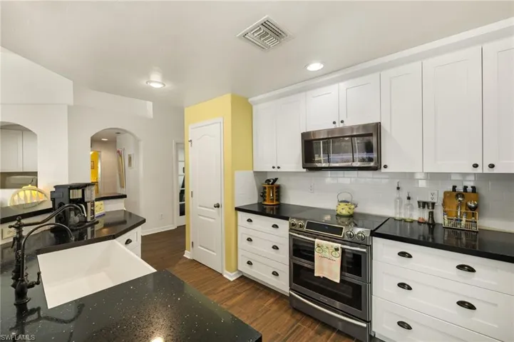 Kitchen with visible vents, dark wood-style floors, appliances with stainless steel finishes, arched walkways, and a sink