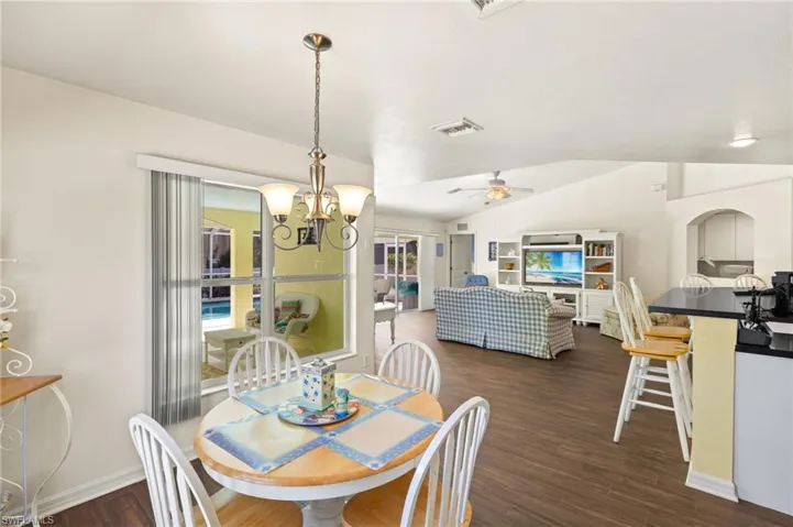 Dining area with visible vents, ceiling fan with notable chandelier, baseboards, lofted ceiling, and dark wood-style flooring