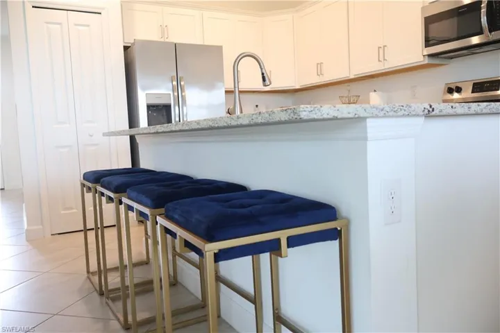 Kitchen featuring stainless steel appliances, white cabinetry, light tile patterned floors, light stone counters, and a breakfast bar