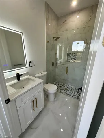 Full bathroom featuring a marble finish shower, toilet, marble finish floor, and vanity