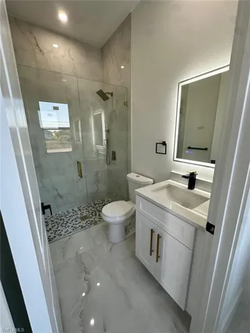 Full bath featuring toilet, a shower stall, marble finish floor, and vanity
