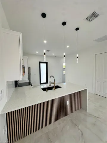 Kitchen with pendant lighting, light stone countertops, white cabinets, visible vents, and a sink