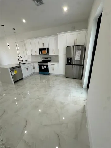 Kitchen featuring a sink, white cabinets, appliances with stainless steel finishes, and marble finish floor